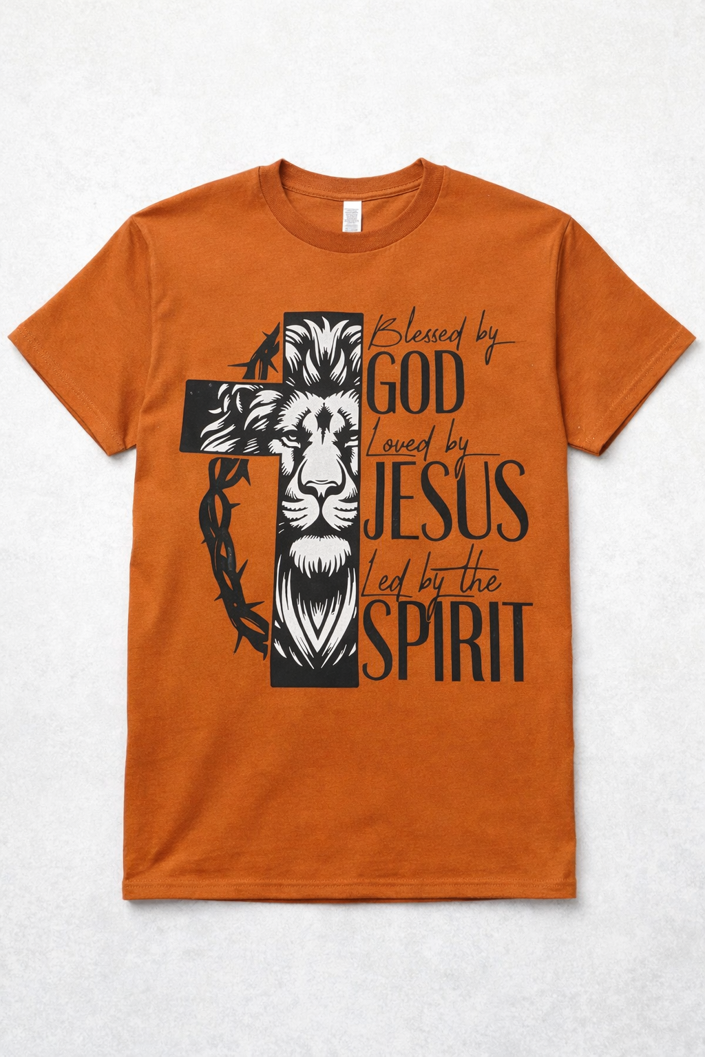 Texas Orange Christian T-Shirt featuring a lion inside a cross with a crown of thorns and the words Blessed by God, Loved by Jesus, Led by the Spirit. Displayed flat with jeans and boots beside it.